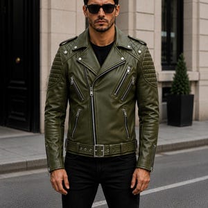 Man wearing olive green leather biker jacket with quilted sleeves, asymmetrical front zipper and belted waist in an urban evening setting.