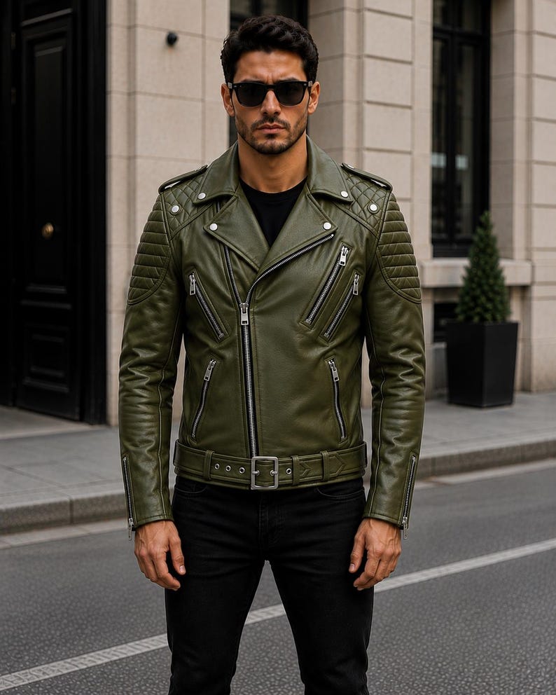 Man wearing olive green leather biker jacket with quilted sleeves, asymmetrical front zipper and belted waist in an urban evening setting.