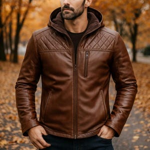 May include: A brown leather hooded jacket featuring a quilted diamond pattern on the upper chest and shoulders, a full-length front zipper, a vertical zippered chest pocket, and two side pockets, worn over a dark shirt.