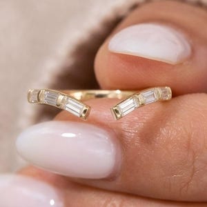Peut inclure: Une bague ouverte en or présentant un design en forme de V orné de plusieurs pierres transparentes taille baguette serties le long de l'anneau. La bague possède une finition métallique polie et un espace au centre, créant un agencement géométrique.