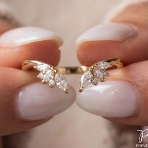 May include: A gold ring with a unique design, featuring a series of marquise-cut and round diamonds. The ring's open design allows it to wrap around the finger, creating a distinctive and elegant look. The diamonds sparkle against the gold setting.