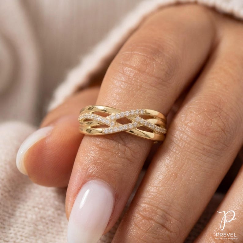 May include: A gold ring with a woven design, featuring small, sparkling stones. The ring is worn on a finger, showcasing its intricate pattern and bright, polished finish. The ring's design is a series of interwoven bands.