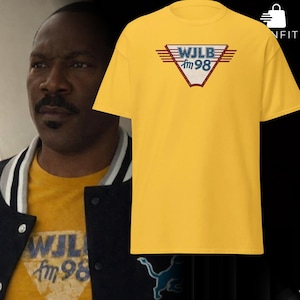 Könnte beinhalten: Ein gelbes T-Shirt mit dem Text "WJLB fm 98" in einem Retro-Design mit roten, blauen und weißen Akzenten. Das Shirt ist ein klassischer Rundhalsausschnitt.