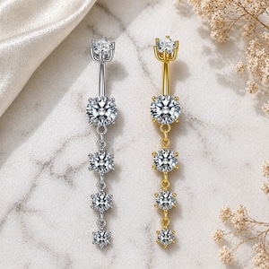 Könnte beinhalten: Zwei Bauchnabelpiercings, eines in Silber und eines in Gold, jeweils mit einer Reihe funkelnder, klarer Edelsteine. Der silberne Ring hat ein vertikales Design mit vier Edelsteinen, während der goldene Ring ein ähnliches Design hat.
