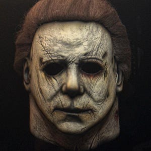 以下が含まれることがあります： 詳細なハロウィーンマスク。顔色は青白く、深いシワと暗い眼窩が特徴です。マスクは茶色の髪とリアルで老いた外観をしています。このマスクは、コスチュームやテーマのあるイベント用の小道具です。