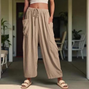 May include: Tan linen-blend wide-leg pants with a drawstring waist and large side pockets. The casual pants are paired with cream-colored sandals. The pants are a neutral color, suitable for various outfits.