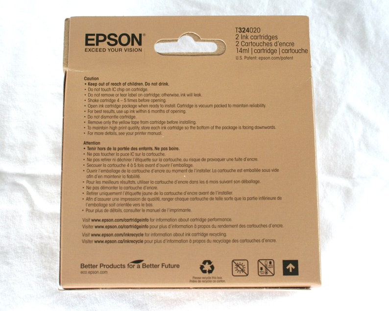K&ouml;nnte beinhalten: Ein brauner Karton mit einem wei&szlig;en Etikett, auf dem "EPSON EXCEED YOUR VISION" steht. Die Schachtel enth&auml;lt zwei 14-ml-Tintenpatronen f&uuml;r Epson-Drucker. Die Schachtel hat ein Warnhinweis-Etikett mit Anweisungen f&uuml;r den sicheren Umgang und die Lagerung der Tintenpatronen.