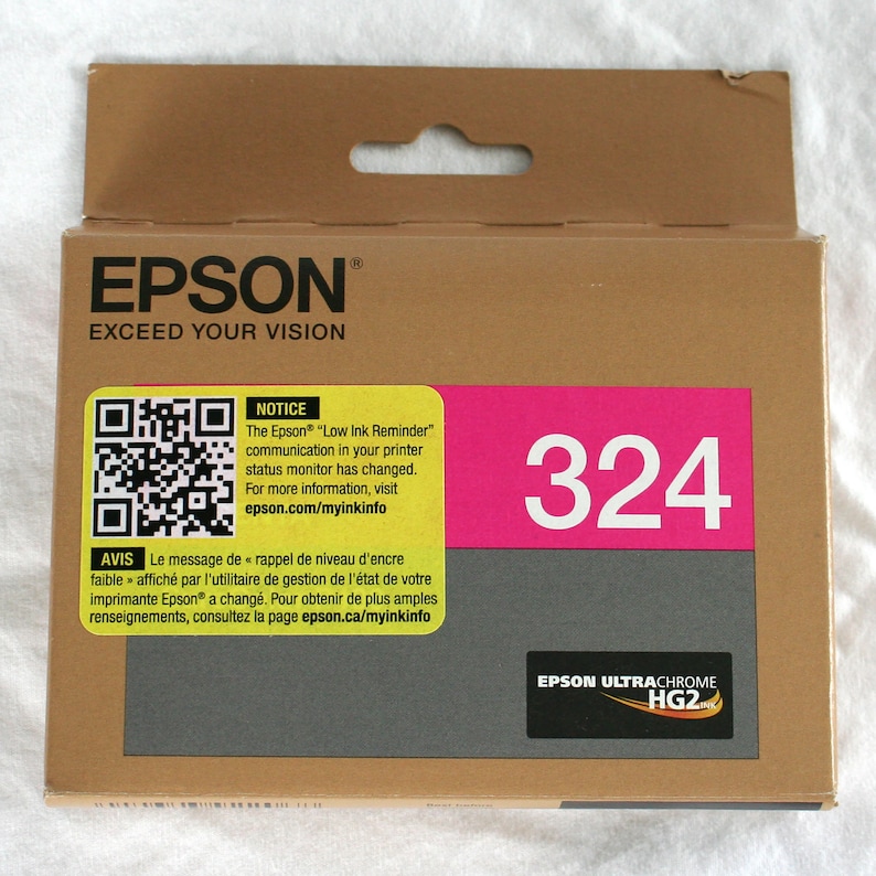 May include: A brown cardboard box of Epson ink cartridges. The box has the Epson logo and the words "EXCEED YOUR VISION". A bright pink rectangle displays the number "324". There is a QR code and a notice about the low ink reminder.
