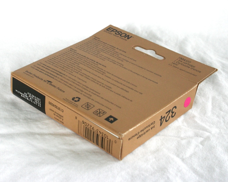 May include: A brown Epson ink cartridge box with the number 324 in black and a pink dot. The box has the text "Ink Cartridge" and "Better Products for a Better Future".