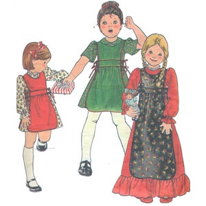 May include: Three girls wearing dresses with different patterns and colors. The girl on the left is holding a wrapped gift. The girl in the middle is wearing a green dress with a white apron. The girl on the right is wearing a red dress with a black apron and is holding a doll.