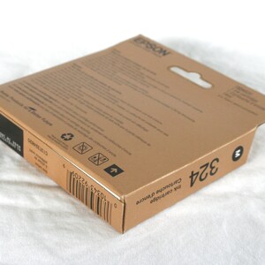 May include: A brown cardboard box with a white label that says "EPSON" and "Ink Cartridge 324". The box has a barcode and a recycling symbol.