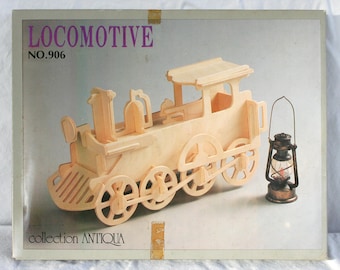 May include: A wooden locomotive model kit with the text "LOCOMOTIVE NO.906" and "collection ANTIQUA" on the box. The kit includes a wooden train and a small metal lantern. The train has large wheels and a detailed design.
