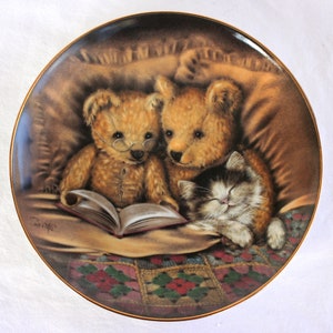 May include: Two teddy bears wearing glasses are reading a book together in bed with a cat sleeping next to them. The bed is covered in a brown blanket and a colorful patchwork quilt.