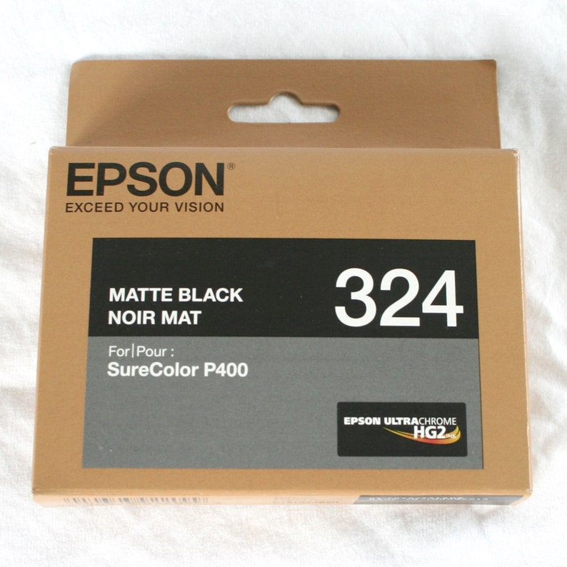 May include: A brown box with a white label that says "EPSON&reg; EXCEED YOUR VISION". The label also says "MATTE BLACK NOIR MAT" and "For Pour: SureColor P400". The box has a white number "324" on it. The box also has a small label that says "EPSON ULTRACHROME HG2".