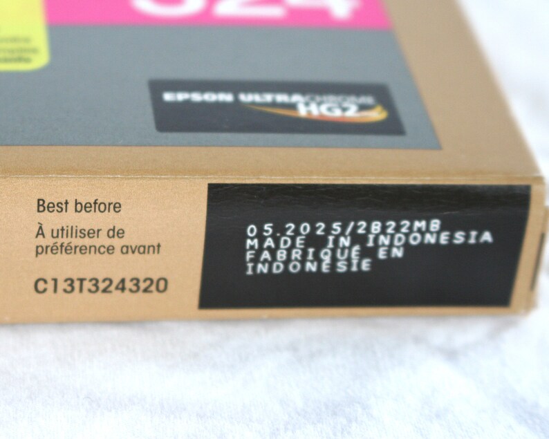 May include: A cardboard box with the text "Best before" and "&Agrave; utiliser de pr&eacute;f&eacute;rence avant". The box also has the text "EPSON ULTRACROME HG2" and "MADE IN INDONESIA". The box is labeled with the code "C13T324320".