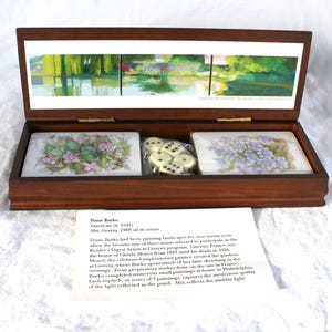 May include: A wooden box with a hinged lid, containing two decorative card decks with floral designs and a set of dice. The box also features a landscape painting on the inside of the lid. The box is made of dark brown wood.