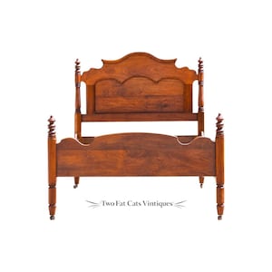 May include: A brown wooden bed frame featuring a headboard and footboard with arched, scalloped top edges. The frame includes four vertical posts with decorative spiral-turned detailing and small wheels at the base. Text reads Two Fat Cats Vintiques.