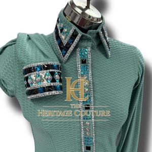 May include: A mint green long-sleeve shirt with a textured pattern. The collar, cuffs, and front placket are embellished with rhinestones and black and blue accents. The text "HERITAGE COUTURE" is visible on the shirt.