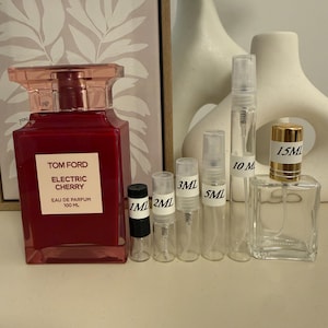 May include: A large red Tom Ford Electric Cherry eau de parfum 100 ml bottle next to a row of clear glass sample spray vials labeled 1 ml, 2 ml, 3 ml, 5 ml, and 10 ml, and a square 15 ml glass perfume bottle with a gold cap.