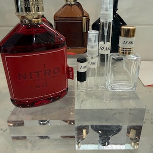 May include: A collection of perfume bottles and sample vials. The primary bottle is red with "NITRO red" text. Other bottles are brown and black, with gold-colored caps. Sample vials are labeled 1 ml, 5 ml, 10 ml, and 15 ml.