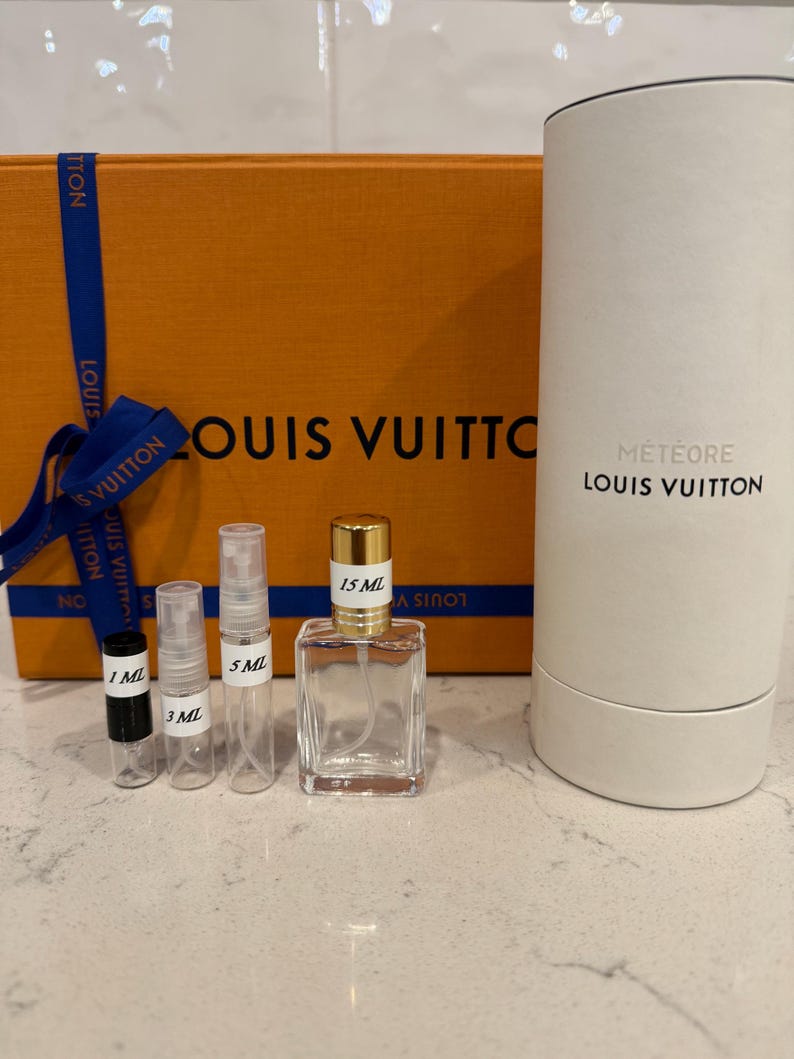 May include: An orange Louis Vuitton box with a blue ribbon, and several perfume bottles. The bottles include sizes 1 ml, 3 ml, 5 ml, and 15 ml. A white cylindrical container with "M&eacute;t&eacute;ore Louis Vuitton" is also present.
