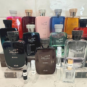 May include: A collection of various perfume bottles in shades of red, pink, blue, and gold, with silver and gold-colored caps. The bottles are labeled with the brand name "HAWAS" and different fragrance names like "BLACK", "ATLANTIS", and "KOBRA".