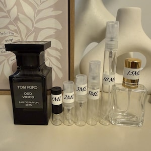 May include: A black Tom Ford Oud Wood 50 ml eau de parfum bottle alongside a row of clear glass spray sample vials labeled 1 ml, 2 ml, 3 ml, 5 ml, 10 ml, and 15 ml. The vials feature white labels with black text indicating their respective capacities.