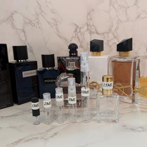 May include: An assortment of perfume bottles and sample vials. The bottles vary in shape and size, with black, gold, and clear caps. Sample vials are labeled with measurements from 1ml to 10ml. The background is a marble-patterned surface.