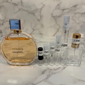 Puede incluir: Un frasco de perfume redondo con el texto "Chance Chanel" y varios peque&ntilde;os frascos pulverizadores transparentes. El frasco de perfume tiene una tapa plateada y contiene un l&iacute;quido naranja claro. Se indican varios tama&ntilde;os.
