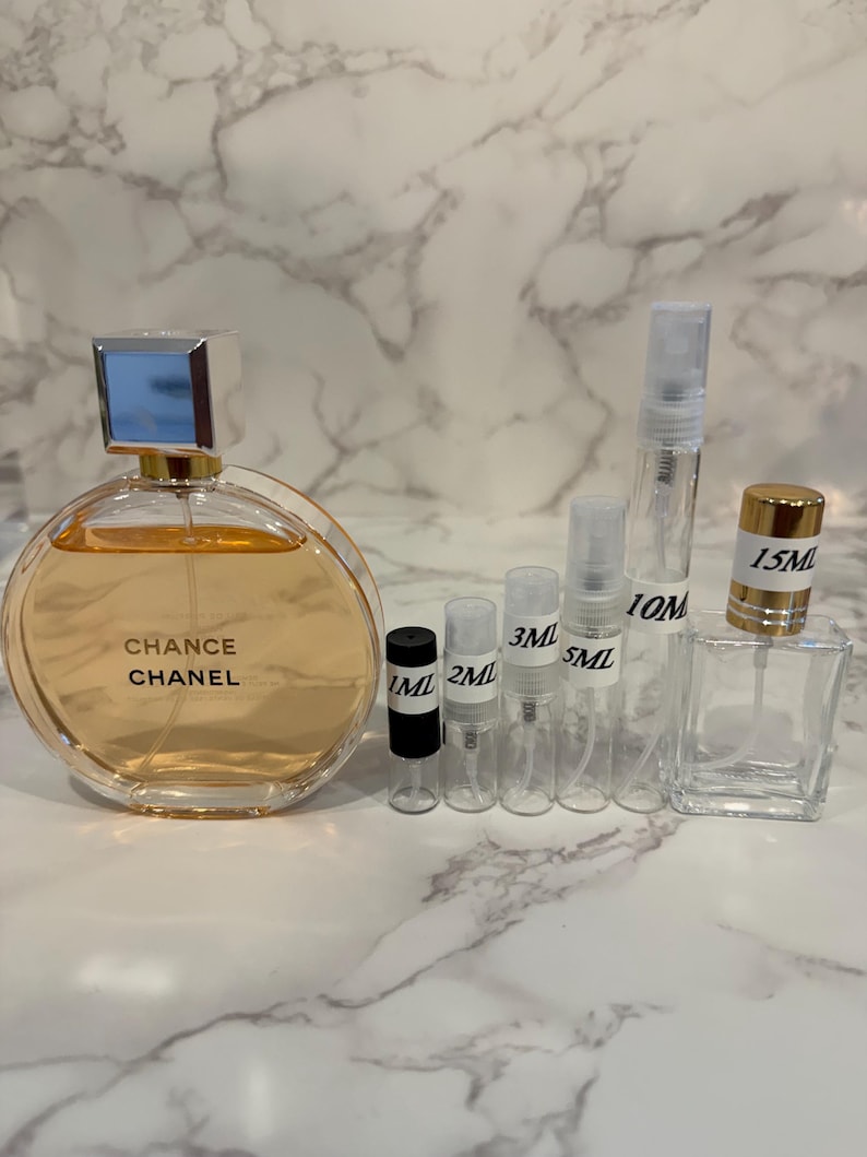 Puede incluir: Un frasco de perfume redondo con el texto "Chance Chanel" y varios peque&ntilde;os frascos pulverizadores transparentes. El frasco de perfume tiene una tapa plateada y contiene un l&iacute;quido naranja claro. Se indican varios tama&ntilde;os.