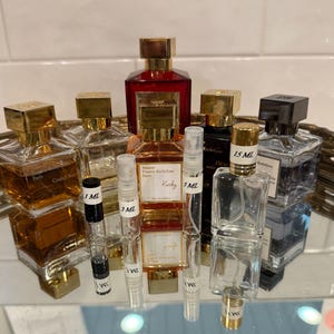 May include: An assortment of perfume bottles and vials with gold and black caps. The bottles vary in size and shape, with labels that read "Paris", "Granil Soir", "Kurky", and "OUD". Vials are labeled 1 ML, 3 ML, and 5 ML.