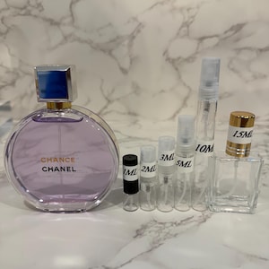 Puede incluir: Una colecci&oacute;n de frascos y atomizadores de perfume. Una botella grande y redonda de color lavanda con una tapa plateada y azul lleva la inscripci&oacute;n "Chance Chanel". Tambi&eacute;n hay varios frascos peque&ntilde;os y transparentes y un frasco cuadrado de vidrio, algunos etiquetados con medidas.