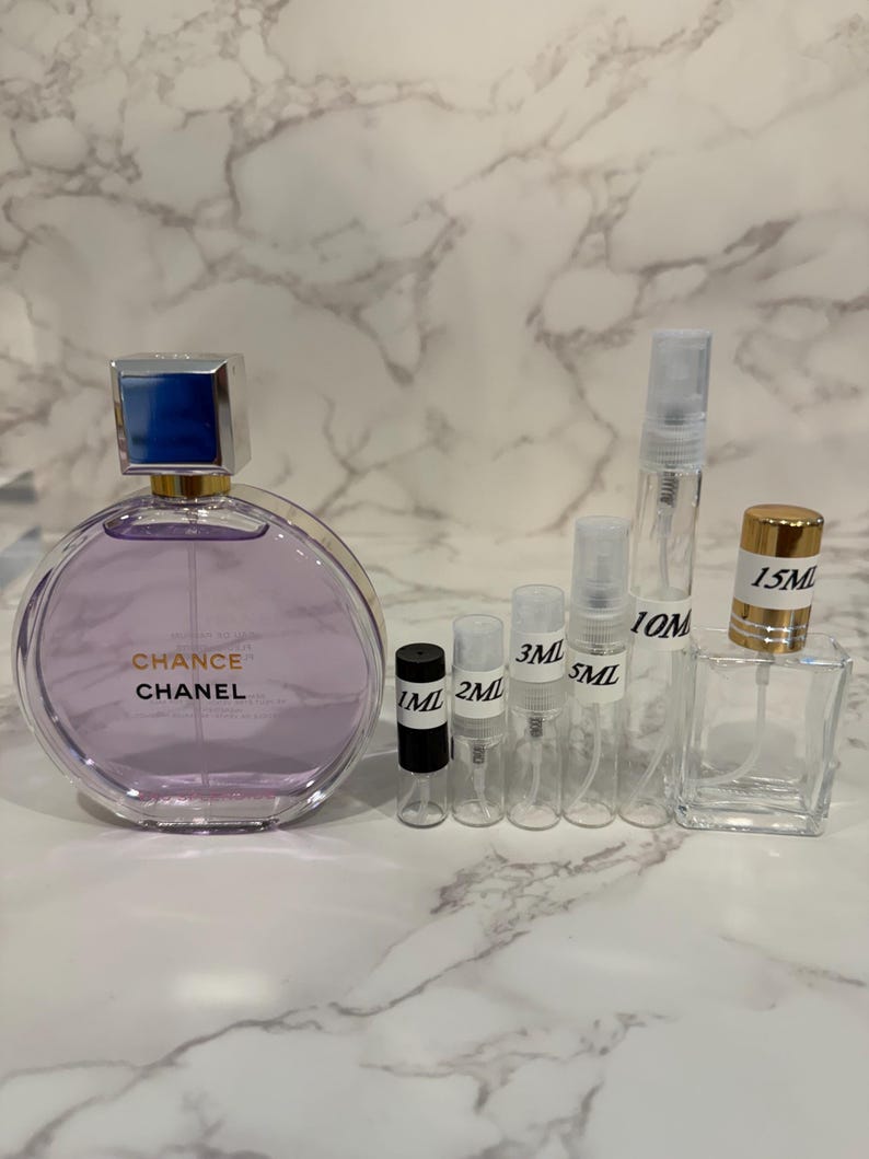Puede incluir: Una colecci&oacute;n de frascos y atomizadores de perfume. Una botella grande y redonda de color lavanda con una tapa plateada y azul lleva la inscripci&oacute;n "Chance Chanel". Tambi&eacute;n hay varios frascos peque&ntilde;os y transparentes y un frasco cuadrado de vidrio, algunos etiquetados con medidas.