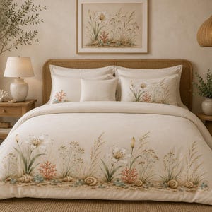 May include: A cream-coloured bedding set featuring a printed design of coastal flora, including white lilies, tall grasses, coral, and seashells along the bottom edge of the duvet cover and on the matching pillow shams, creating a nature-inspired look.