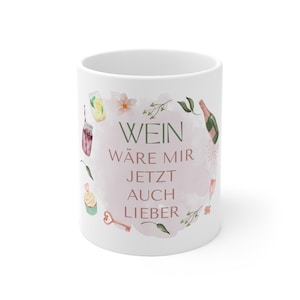 以下が含まれることがあります： ドイツ語のテキスト「WEIN WÄRE MIR JETZT AUCH LIEBER」が緑色で書かれた白いセラミックマグ。ワイン関連のアイテムの水彩イラストで囲まれています。マグカップはピンク色の水彩画の背景が特徴です。
