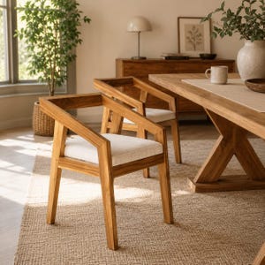 Puede incluir: Una silla de comedor de madera con un cojín de asiento tapizado en color claro. La silla presenta una estructura geométrica con reposabrazos inclinados y patas rectas, fabricada en madera de tonos cálidos con veta visible.