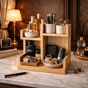 May include: A light oak organiser with compartments for perfume, watches, a wallet, and grooming items. The organiser is on a marble surface. A lamp and other decorative items are in the background.