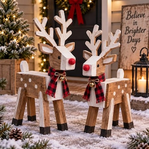 May include: Two rustic wooden reindeer figurines featuring white-painted antlers, bodies with white polka dots, and black-painted hooves. Each reindeer wears a red and black buffalo plaid scarf with a small gold bell tied around the neck.