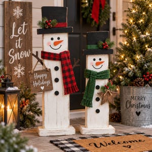 Peut inclure: Deux bonhommes de neige en bois avec des corps blancs, des chapeaux hauts-de-forme noirs et des nez en carotte orange. Le plus grand porte une écharpe à carreaux rouges et noirs et tient un panneau Happy Holidays. Le plus petit a une écharpe verte.