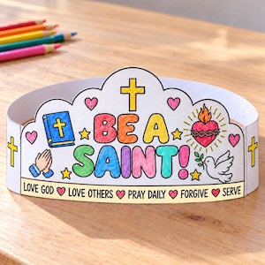 May include: A paper crown featuring the text BE A SAINT! in colorful letters, surrounded by illustrations of a blue Bible, a flaming heart, a white dove, and praying hands. The base includes the text LOVE GOD, LOVE OTHERS, PRAY DAILY, FORGIVE, SERVE.