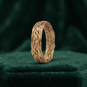 Peut inclure: Une bague en or rose présentant un design complexe en fil tressé rappelant un nid d'oiseau. L'anneau est composé de multiples brins métalliques fins et entrelacés qui créent une apparence texturée et organique avec une finition polie.