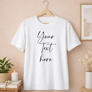 May include: A white t-shirt with the words "Your Text here" in black script. The shirt is hanging on a wooden hanger against a neutral background. The t-shirt is a classic crew neck style.