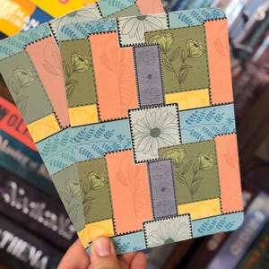Peut inclure: Une pile de marque-pages à motifs floraux avec un motif patchwork. Les marque-pages présentent une variété de couleurs, dont le pêche, le vert, le bleu et le jaune, avec des illustrations florales et de feuilles. Les bords sont festonnés.