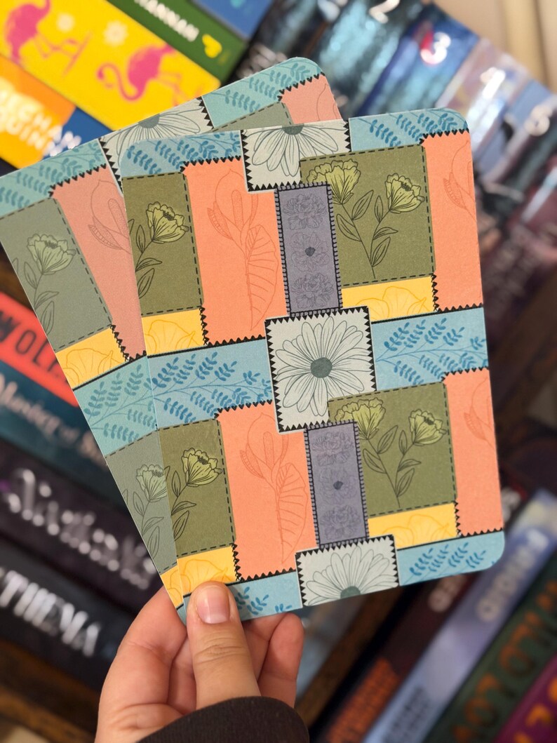 Puede incluir: Una pila de marcadores con estampado floral con un dise&ntilde;o de patchwork. Los marcadores presentan una variedad de colores, incluyendo melocot&oacute;n, verde, azul y amarillo, con ilustraciones florales y de hojas. Los bordes son festoneados.