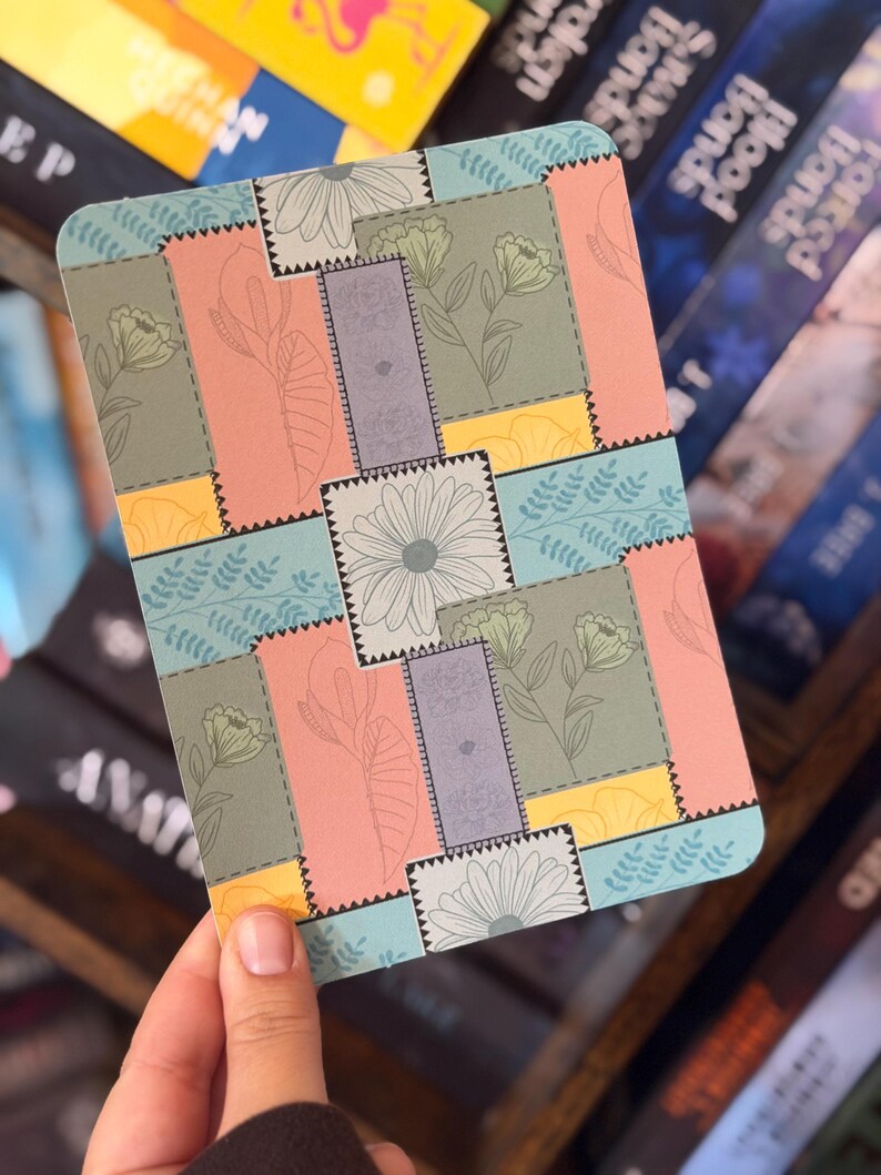 Puede incluir: Un posavasos rectangular con un dise&ntilde;o de patchwork que presenta ilustraciones florales y de hojas en colores pastel. El posavasos tiene una combinaci&oacute;n de colores azul claro, rosa, amarillo y verde, con un borde gris y una margarita blanca.