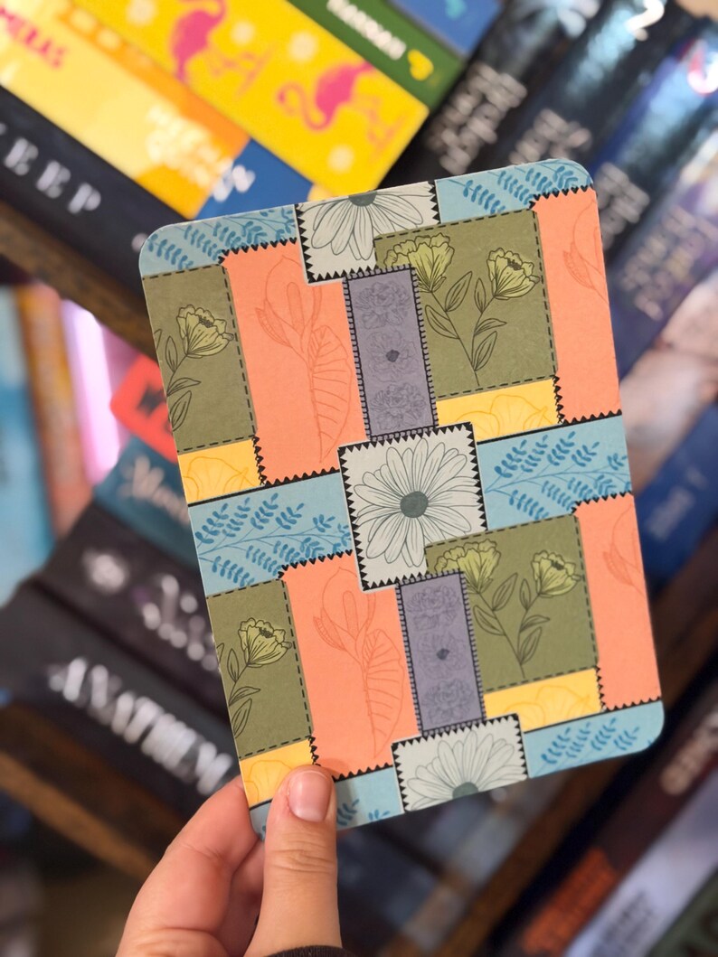 Puede incluir: Un cuaderno rectangular con un dise&ntilde;o floral de patchwork. El dise&ntilde;o presenta varios colores, incluyendo naranja, verde, azul y amarillo, con ilustraciones florales y de hojas. El cuaderno est&aacute; en la mano de una persona.