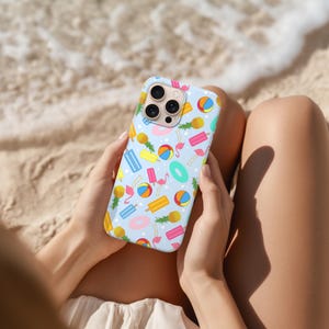 Könnte beinhalten: Hellblaue Handyhülle mit einem sommerlichen Muster. Das Design umfasst Illustrationen von Ananas, Eis am Stiel, Strandbällen, Flamingos und aufblasbaren Ringen. Die Hülle wird von einer Person an einem Sandstrand gehalten.