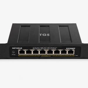 Può includere: Switch di rete NETGEAR GS308EP nero con più porte Ethernet. Lo switch ha un indicatore di alimentazione e un indicatore di carico massimo. Il testo "NETGEAR" e "GS308EP" è sul pannello frontale.