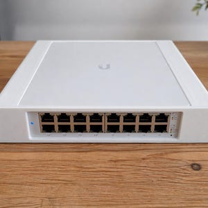 May include: A white network switch with multiple Ethernet ports. The device has a clean, minimalist design with a rectangular shape and a series of ports across the front. The brand logo is visible on the top. The switch is designed for network connectivity.