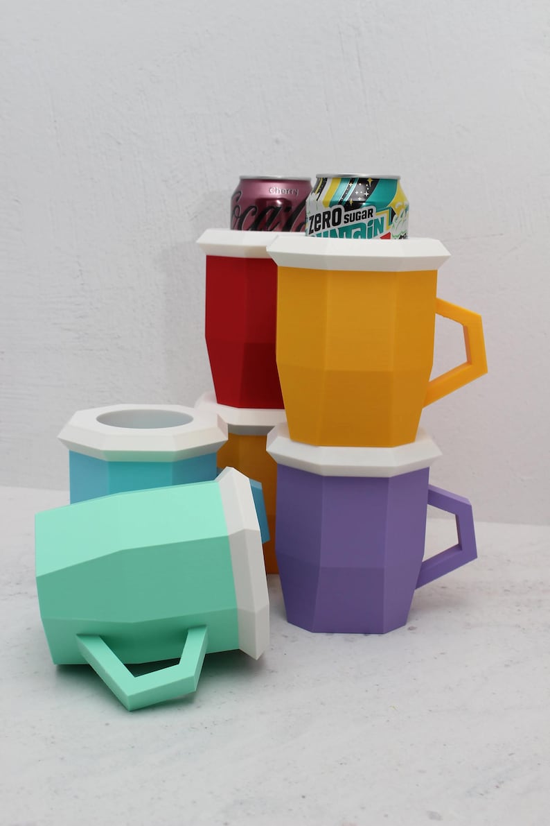 May include: A collection of geometric, faceted beverage holders in red, yellow, purple, light blue, and mint green, each featuring a white rim and angular handle. Two aluminium soda cans are visible inside the red and yellow holders.